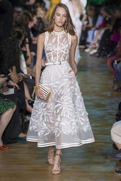 a model walks down the runway in a white dress with flowers on it and gold accessories