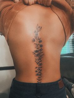 the back of a woman's lower back tattoo with flowers and leaves on it