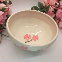 a white bowl with pink flowers on it and a branch painted on the side, sitting next to some pink roses