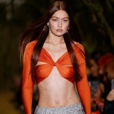 a woman in an orange top is walking down the runway