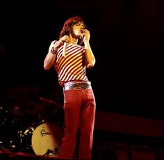 a man in striped shirt and red pants holding a microphone up to his ear while standing on stage