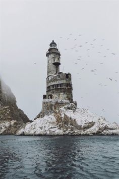 a large tower sitting on top of a snow covered mountain next to the ocean with birds flying over it