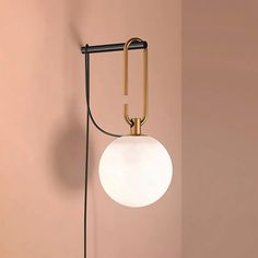 a wall light with a white ball hanging from it's side against a pink wall