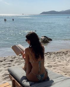 a woman sitting on top of a beach next to the ocean while reading a book