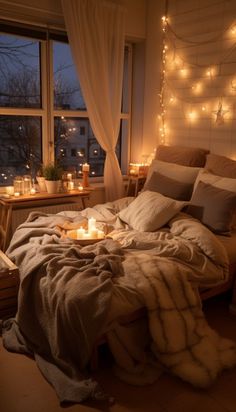 an unmade bed with candles and blankets on it in front of a large window