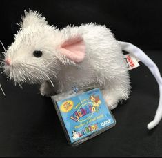 a white stuffed animal mouse sitting on top of a black table next to a tag