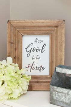 a wooden frame sitting on top of a white shelf next to a vase with flowers