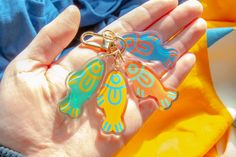 a person holding three different colored fish shaped key chains