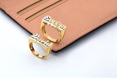 two gold rings sitting on top of a pink leather wallet with the word love spelled in cursive letters
