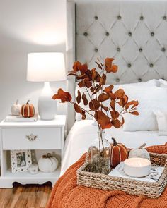 a white bed topped with a basket filled with pumpkins and a vase full of flowers