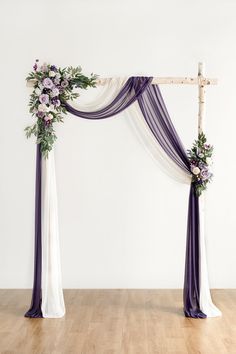 an arch decorated with purple and white flowers on top of a wooden floor next to a wall