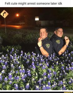 two police officers standing next to each other in front of blue flowers at night time