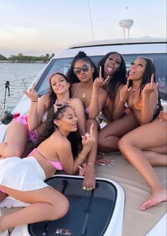 four women in bikinis posing on the back of a boat with their fingers up