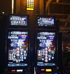 two slot machines sitting next to each other in front of a wall mounted tv screen