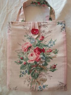 a pink bag with flowers on it sitting on a white sheet covered bed next to a red button