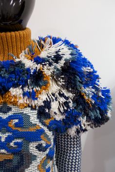 a mannequin wearing a colorful knitted sweater with fringes on it's shoulders