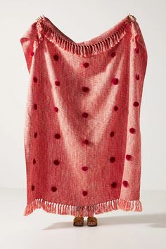 a pink blanket with red polka dots and tassels on the edges, hanging from a white wall