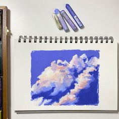 three markers are sitting on top of a drawing book next to some pens and watercolors