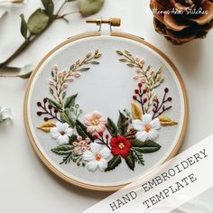 an embroidery project with flowers and leaves on the hoop, next to a pine cone