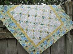 a quilt hanging on the side of a wooden fence next to a green and yellow tree