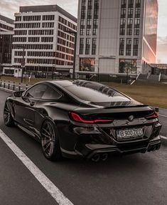 a black sports car driving down the road in front of some tall buildings at sunset