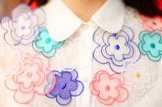 a woman with red hair wearing a white shirt and colorful flower appliques on her collar