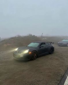 two cars are parked in the dirt on a foggy day