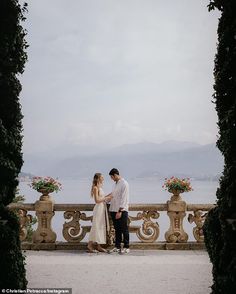 a man and woman standing next to each other in front of an arch with flowers on it