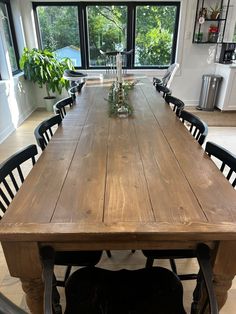 a large wooden table with black chairs in front of a window and potted plant