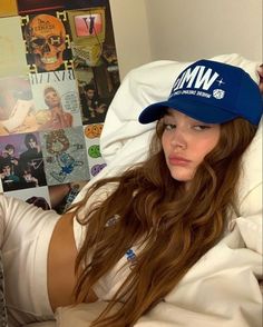 a woman with long hair wearing a hat and sitting on a bed in front of posters