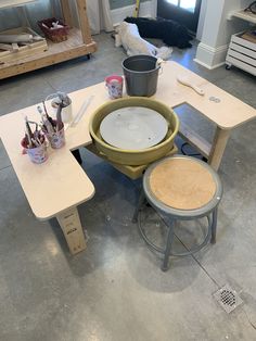an unfinished table and stools in a room with tools on the table, including paintbrushes