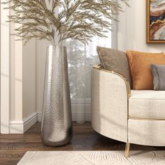 a silver vase sitting on top of a wooden floor next to a white couch and chair