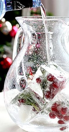 a glass pitcher filled with ice and cherries on top of a table next to a christmas tree