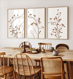 a dining room table with four chairs and two paintings on the wall above it that have flowers in them