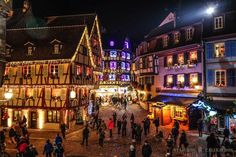 people are walking through an old town at christmas time with lights and decorations on the buildings