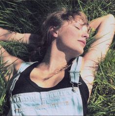 a woman laying in the grass with her head resting on her hands and eyes closed