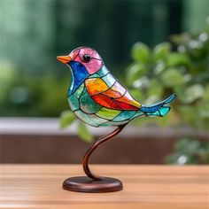 a colorful glass bird sitting on top of a wooden table next to a potted plant