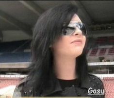 a woman with long black hair and sunglasses in front of an empty bleachers