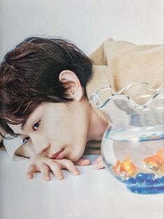 a young man laying on the floor next to a fish bowl with goldfish in it