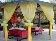 an outdoor picnic area with yellow drapes and red table cloths, blue tables and balloons