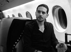 a man sitting on an airplane seat holding a glass in his hand and looking at the camera