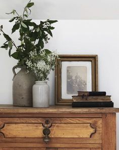 there is a vase with flowers on top of a dresser next to a framed photograph