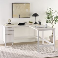 a white desk with two drawers and a lamp on it next to a potted plant