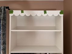 a white shelf with green trim on the top and two shelves below it, in front of a window