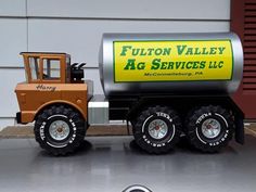 a toy truck with a fuel tank on it's flatbed is parked in front of a garage