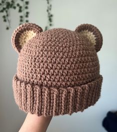 a hand holding up a brown knitted bear hat