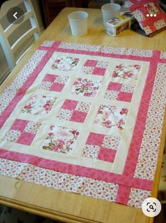 a table with a pink and white quilt on it's top, next to some cups