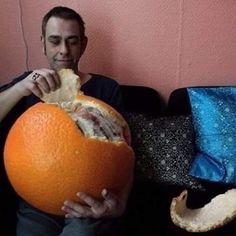a man sitting on a couch holding an orange