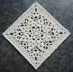 a white crocheted square sitting on top of a black table next to a gray surface