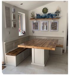 a wooden table sitting in the middle of a room with pictures on the wall above it